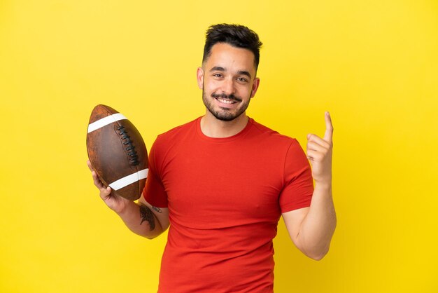 Joven caucásico jugando al rugby aislado sobre fondo amarillo apuntando hacia una gran idea