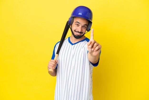 Joven caucásico jugando béisbol aislado sobre fondo amarillo mostrando y levantando un dedo