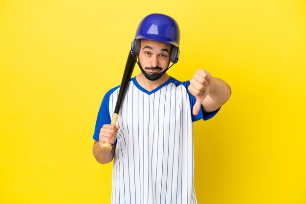 Joven caucásico jugando béisbol aislado sobre fondo amarillo mostrando el pulgar hacia abajo con expresión negativa