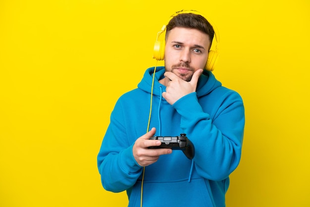 Joven caucásico jugando con un controlador de videojuegos aislado en un pensamiento de fondo amarillo