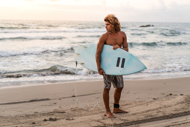 Joven caucásico levantarse temprano para hacer surf al amanecer.