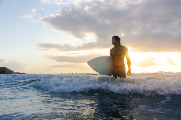 Joven caucásico levantarse temprano para hacer surf al amanecer.