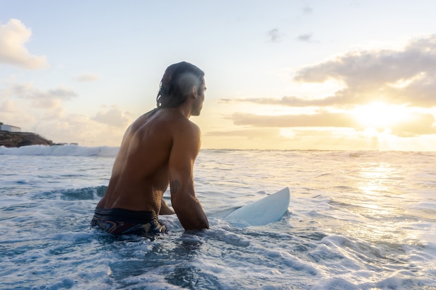 Joven caucásico levantarse temprano para hacer surf al amanecer.