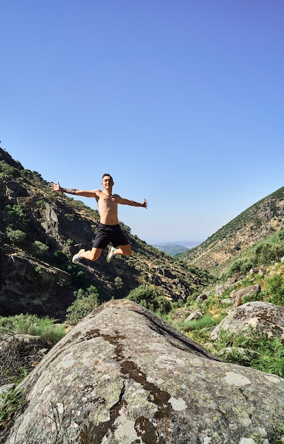 Foto joven caucásico, libre y feliz, saltando con los brazos abiertos en un hermoso paisaje de montañas.