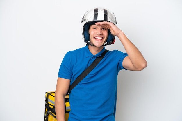 Joven caucásico con mochila térmica aislada de fondo blanco mirando lejos con la mano para mirar algo