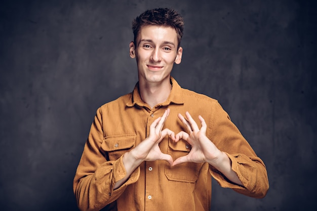 Joven caucásico mostrar gesto de corazón sobre fondo gris oscuro