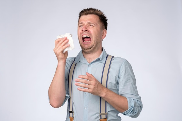 Joven caucásico con pañuelo estornudando Estar enfermo con gripe o alergia Foto de estudio