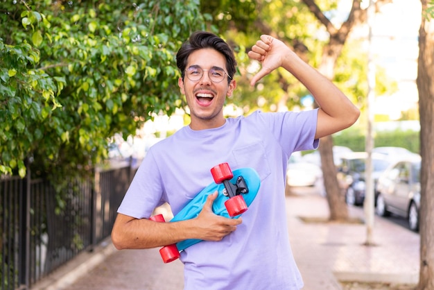 Joven caucásico en un parque con un patín con expresión feliz