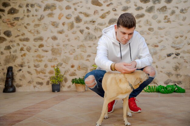 Joven caucásico en el patio trasero con un perro En el fondo hay una pared de piedras