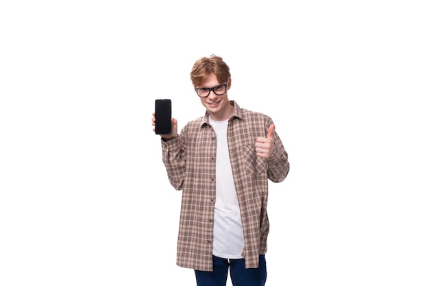 Un joven caucásico con pelo rojo, gafas y una camisa a cuadros muestra la pantalla de un teléfono inteligente