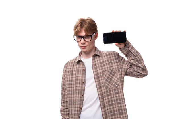 Un joven caucásico con pelo rojo y gafas muestra la pantalla del teléfono inteligente