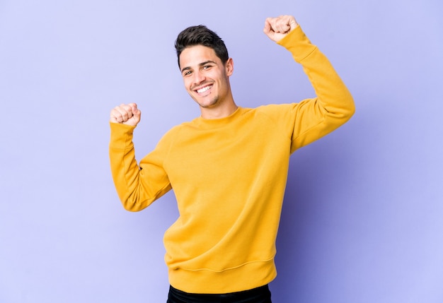 Joven caucásico en púrpura celebrando un día especial, salta y levanta los brazos con energía.