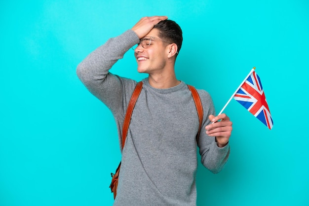 Un joven caucásico que sostiene una bandera del Reino Unido aislada de fondo azul se ha dado cuenta de algo y tiene la intención de encontrar la solución
