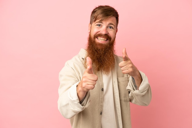 Joven caucásico rojizo aislado de fondo rosa apuntando al frente y sonriendo