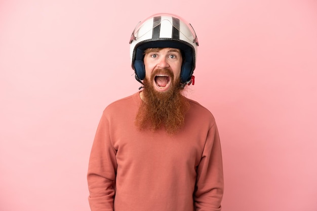 Joven caucásico rojizo con casco de motocicleta aislado de fondo rosa con expresión facial sorpresa