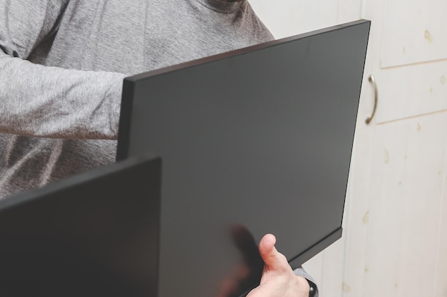 Un joven caucásico sin rostro sostiene un monitor de computadora con las manos