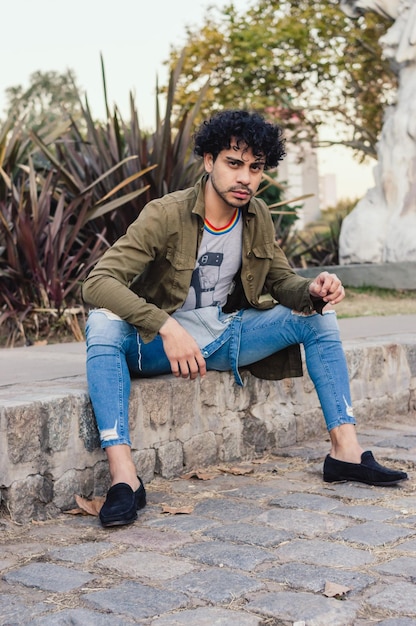 Joven caucásico con rulos al aire libre posando sentado en el parque