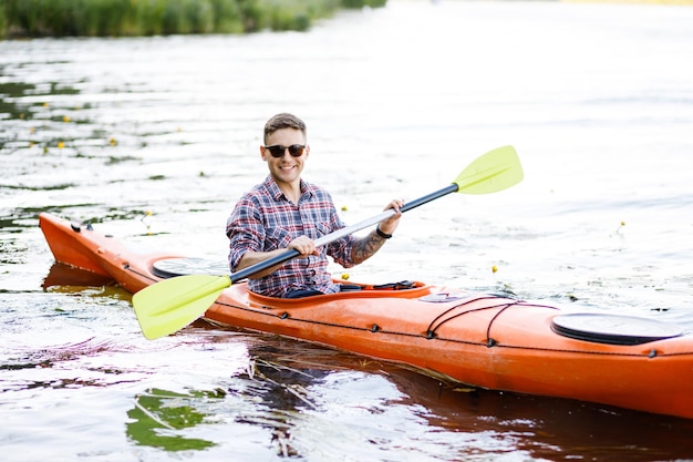 Un joven caucásico se sienta en un kayak y rema El concepto de entretenimiento acuático