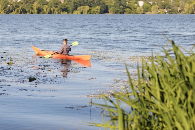 Un joven caucásico se sienta en un kayak y rema El concepto de entretenimiento acuático