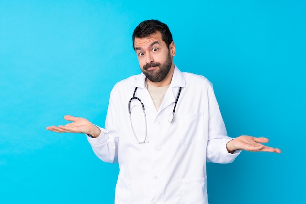 Foto joven caucásico sobre pared aislada vistiendo una bata de médico y teniendo dudas