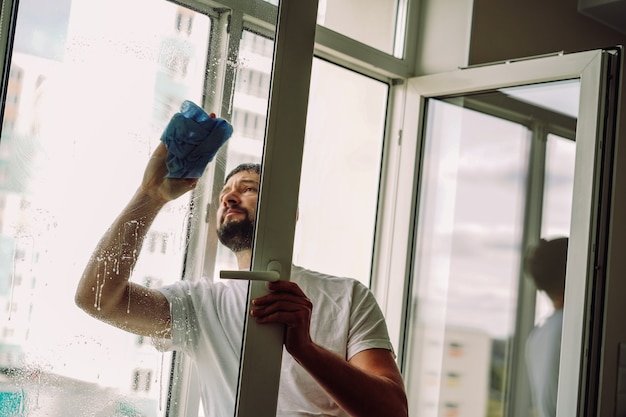 joven, caucásico, sonriente, hombre, lavar la ventana, con, un, escobilla de goma, concepto