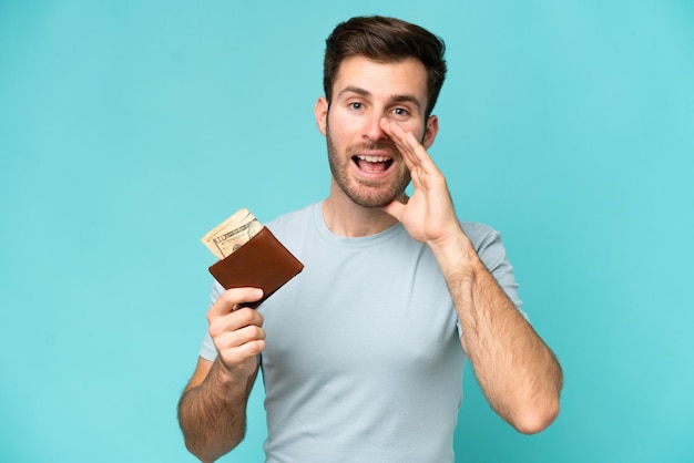 Joven caucásico sosteniendo una billetera aislada de fondo azul gritando con la boca abierta