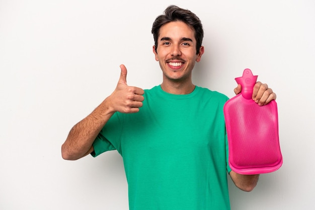 Joven caucásico sosteniendo una bolsa de agua aislada de fondo blanco sonriendo y levantando el pulgar