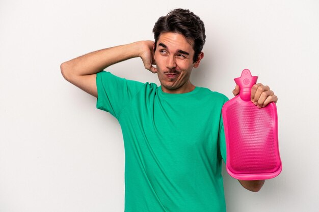 Foto joven caucásico sosteniendo una bolsa de agua aislada de fondo blanco tocando la parte posterior de la cabeza, pensando y tomando una decisión.