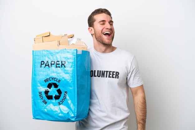 Joven caucásico sosteniendo una bolsa de reciclaje llena de papel para reciclar aislado sobre fondo blanco riendo