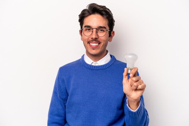 Joven caucásico sosteniendo una bombilla aislada de fondo blanco feliz, sonriente y alegre.