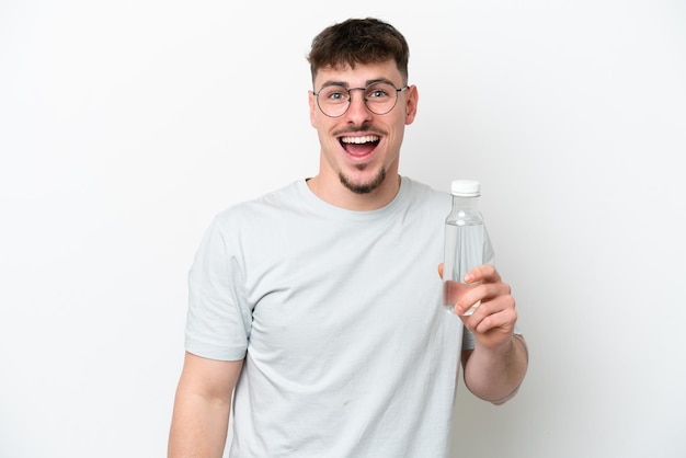 Joven caucásico sosteniendo una botella de agua aislada de fondo blanco con expresión facial sorprendida y sorprendida