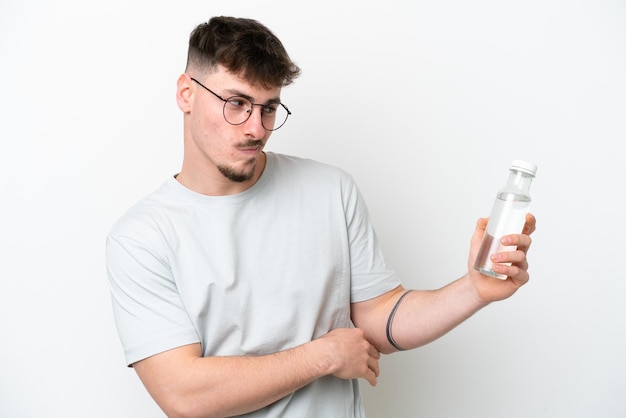 Joven caucásico sosteniendo una botella de agua aislada de fondo blanco con expresión triste