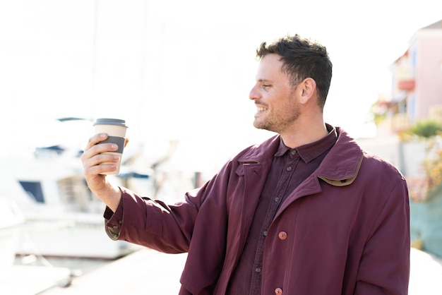 Foto joven caucásico sosteniendo un café para llevar al aire libre con expresión feliz