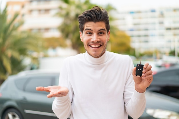 Joven caucásico sosteniendo las llaves del auto al aire libre con una expresión facial sorprendida