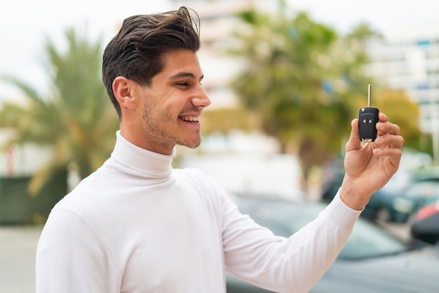 Joven caucásico sosteniendo las llaves del auto al aire libre con expresión feliz