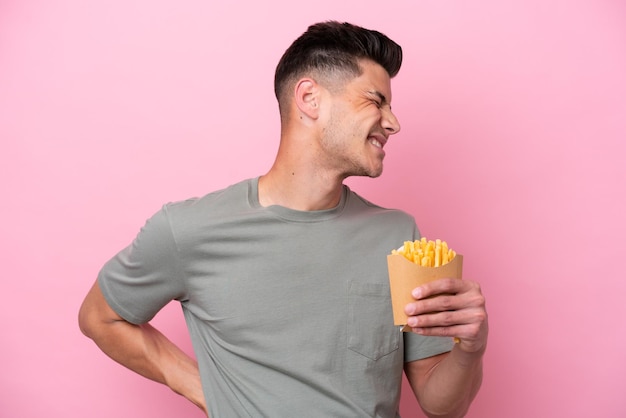 Joven caucásico sosteniendo papas fritas aisladas en un fondo rosado que sufre de dolor de espalda por haber hecho un esfuerzo