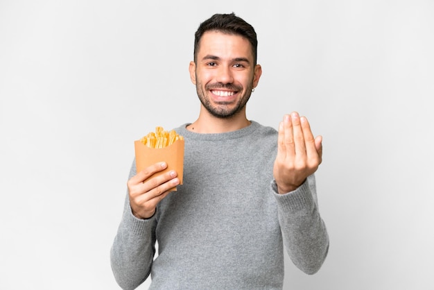 Joven caucásico sosteniendo papas fritas sobre fondo blanco aislado invitando a venir con la mano feliz de que hayas venido