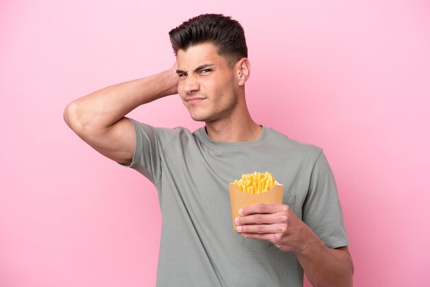 Joven caucásico sosteniendo patatas fritas aisladas de fondo rosa con dudas