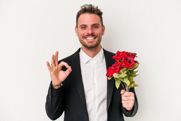 Joven caucásico sosteniendo un ramo de flores aislado en un fondo blanco alegre y confiado mostrando un gesto correcto.