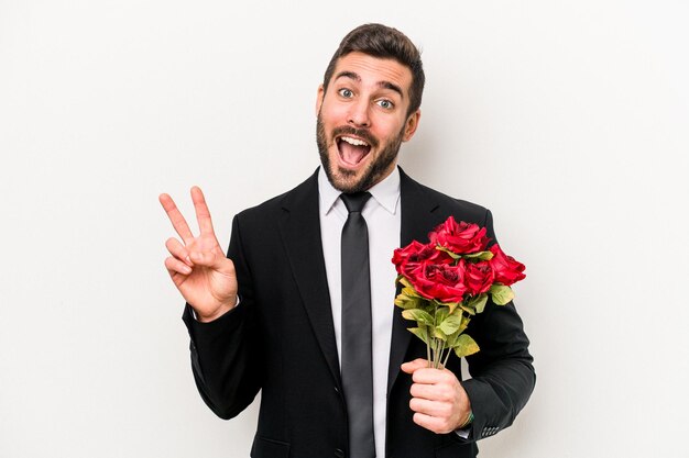 Joven caucásico sosteniendo un ramo de flores aislado de fondo blanco alegre y despreocupado mostrando un símbolo de paz con los dedos