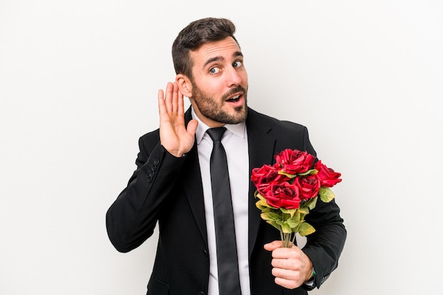 Joven caucásico sosteniendo un ramo de flores aislado de fondo blanco tratando de escuchar un chisme