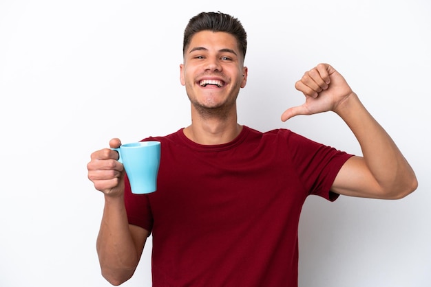 Joven caucásico sosteniendo una taza de café aislado de fondo blanco orgulloso y satisfecho de sí mismo