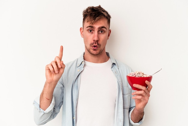 Joven caucásico sosteniendo un tazón de cereales aislado sobre fondo blanco con una gran idea, concepto de creatividad.