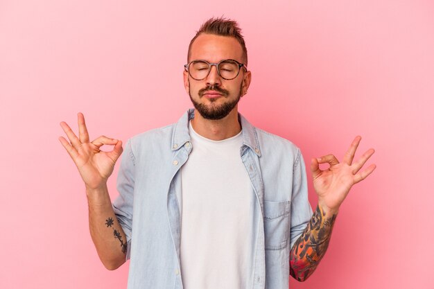 Joven caucásico con tatuajes aislados sobre fondo rosa se relaja después de un duro día de trabajo, ella está realizando yoga.