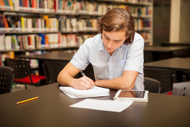 Joven caucásico tomando algunas notas y haciendo la tarea en la biblioteca de la escuela