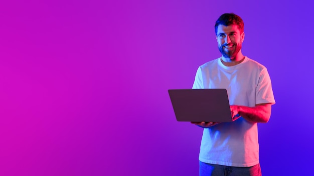 Un joven caucásico usando una computadora portátil en un estudio con luz de neón