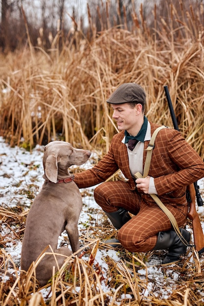 Un joven cazador europeo caucásico con traje se sienta con un perro en el campo y se dirige al hombre guapo