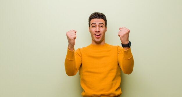 Joven celebrando un éxito increíble como un ganador, con expresión emocionada y feliz diciendo: ¡Toma eso! sobre pared