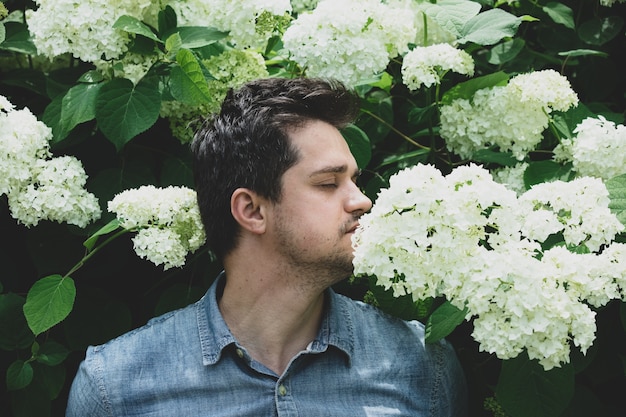 Joven cerca de arbusto de flores blancas en un jardín.