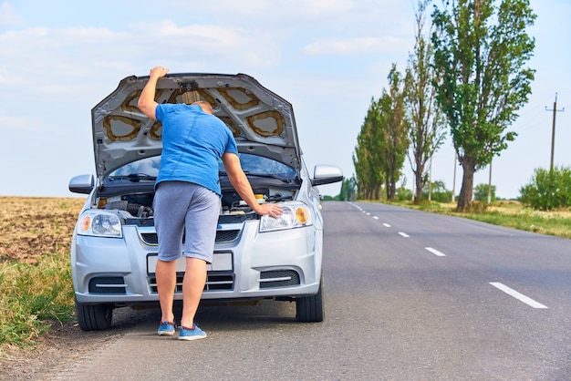 Un joven cerca del automóvil con el capó abierto al costado de la carretera.